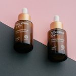 Two dropper bottles of Sesderma C-Vit liposomal serum on a pink and gray background.