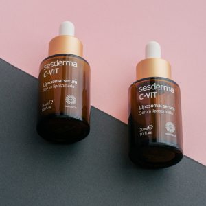 Two dropper bottles of Sesderma C-Vit liposomal serum on a pink and gray background.