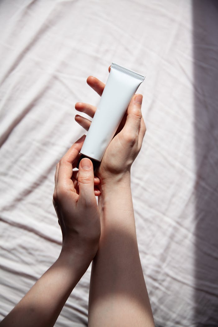 Close-up of hands holding a cosmetic tube against a bright, textured background.