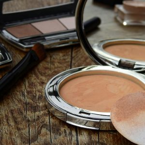 Close-up of makeup tools including compact, brush, and mirror on a rustic wooden surface.