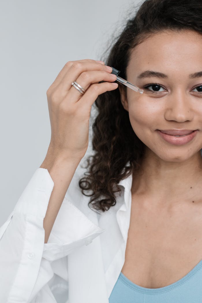 Close-up of a young woman applying skincare product with a dropper, focusing on self-care and beauty.