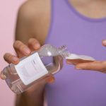 Woman applying skincare tonic with a cotton pad. Focus on hands and product in a studio setting.