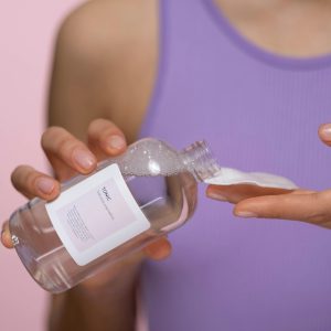 Woman applying skincare tonic with a cotton pad. Focus on hands and product in a studio setting.